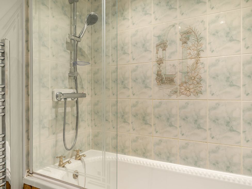 A bathtub with shower fixtures and tiled wall featuring decorative floral and architectural design at Brant View in Cautley near Sedbergh