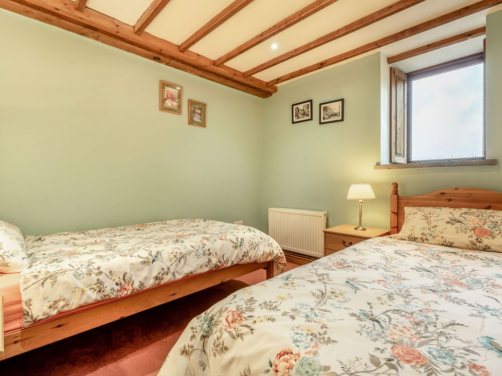 A bedroom with two beds floral bedding a wooden nightstand with a lamp a window and framed pictures on the walls at Brant View in Cautley near Sedbergh