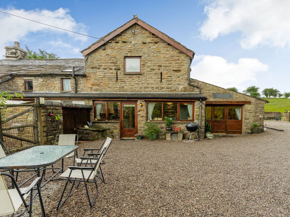A stone house with wooden doors and windows and a gravel patio with a glass table and chairs at Brant View in Cautley near Sedbergh