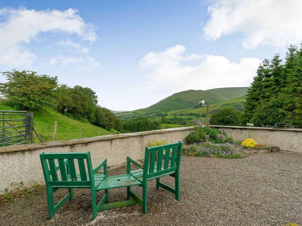An outdoor patio with green connected chairs overlooking a garden and hills at Brant View in Cautley near Sedbergh