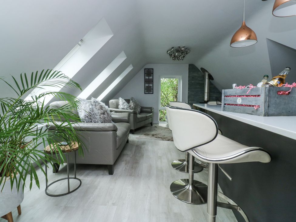 A living area with sofas and bar stools with a plant by a window at Treetops in Southerton