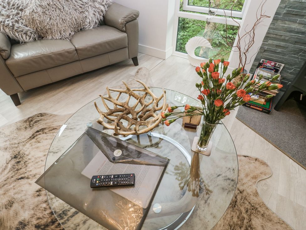 A living room with a glass coffee table holding a remote control flowers and antler decor at Treetops in Southerton