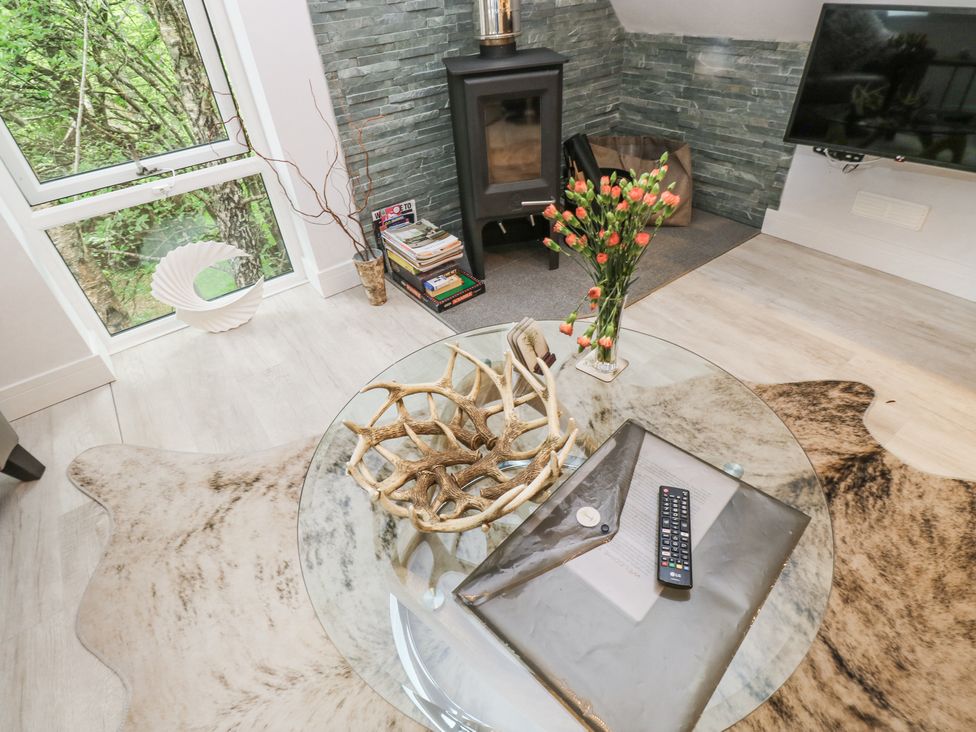 A living room with a glass coffee table holding a remote control and flowers near a fireplace and window at Treetops in Southerton