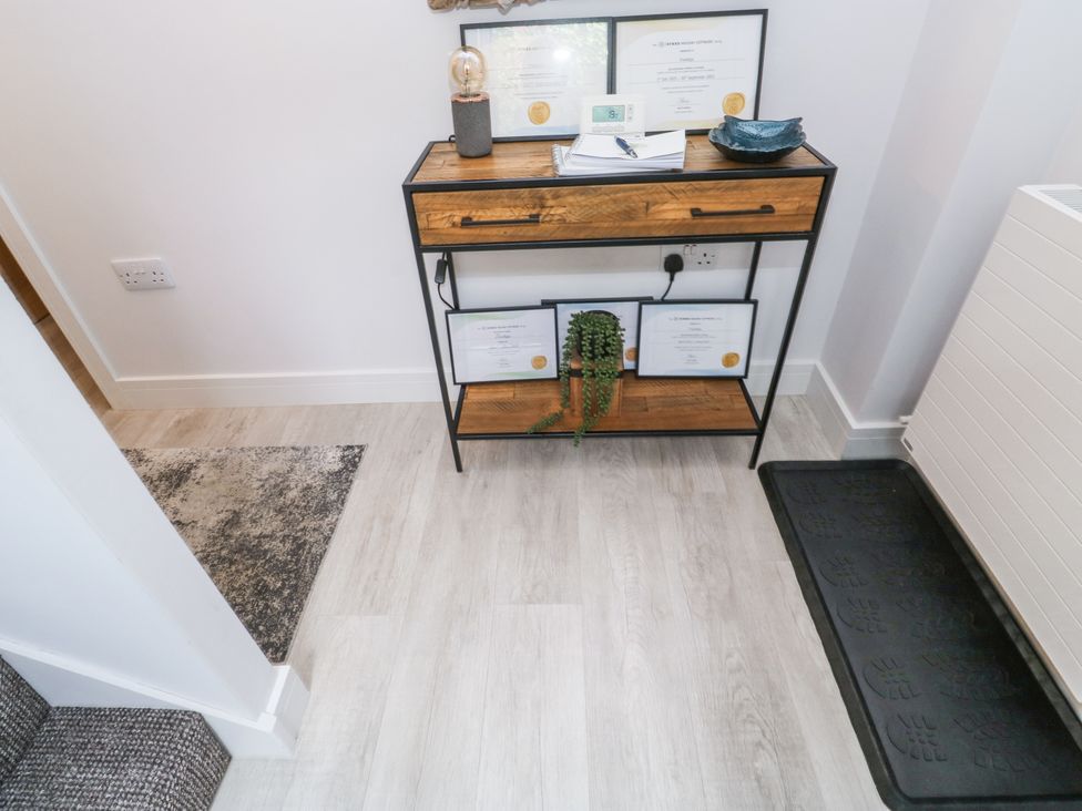 A hallway with a wooden console table holding framed certificates a lamp a thermostat and a plant at Treetops in Southerton