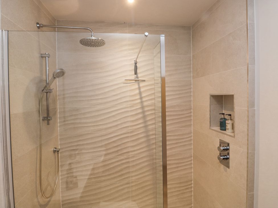 A shower area with a rainfall showerhead a handheld showerhead and two bottles in a wall niche at Treetops in Southerton