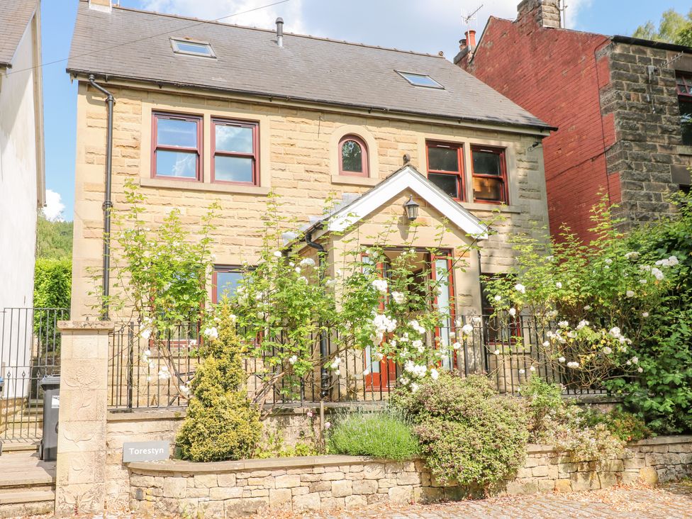 A stone two-story house with red window frames and a small garden with white flowers at Torestyn in Darley Dale