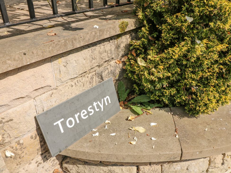 A stone ledge with a sign reading Torestyn surrounded by a bush and fallen leaves at Torestyn Darley Dale