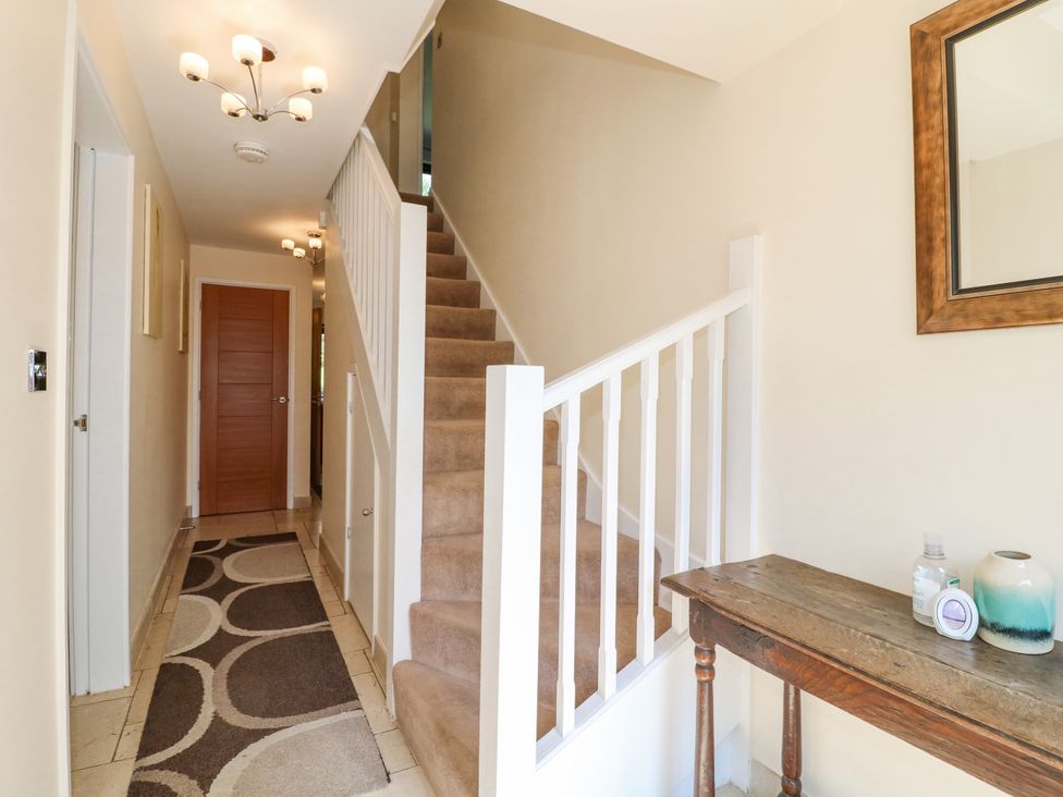 A hallway with carpeted stairs a runner rug a wooden table with decorative items and a mirror at Torestyn in Darley Dale