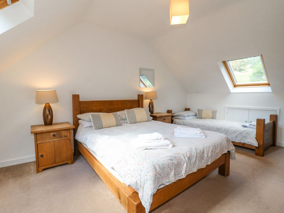 A bedroom with a double bed and a single bed with wooden frames a pair of bedside tables with lamps and a skylight window at Torestyn in Darley Dale