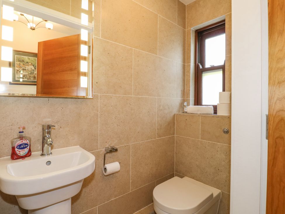 A bathroom with a sink soap dispenser mirror toilet and a window at Torestyn in Darley Dale
