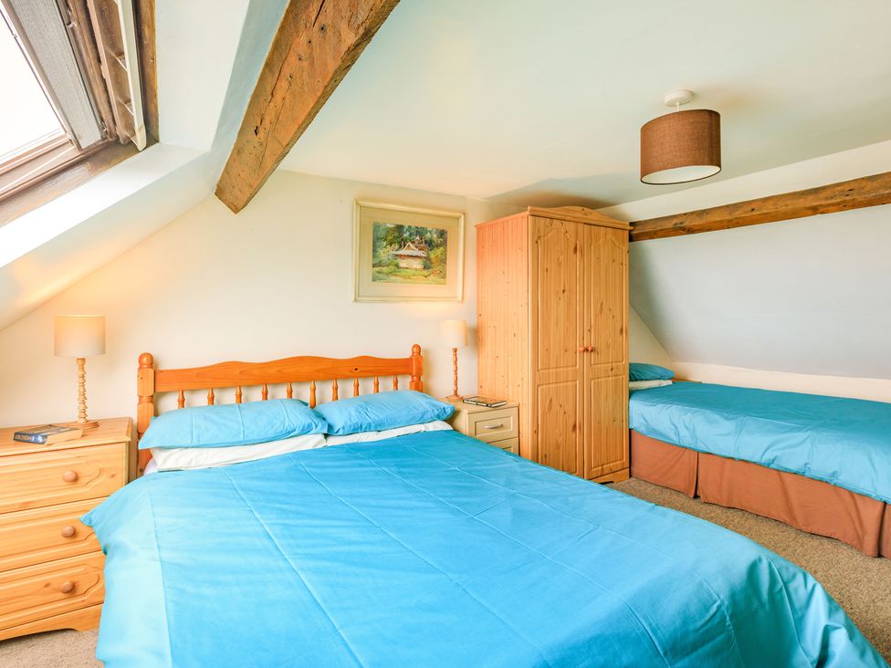 A bedroom with two beds a wooden wardrobe two bedside tables with lamps and a painting on the wall at Hillymouth in Ilfracombe