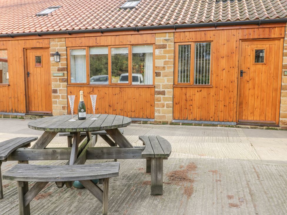A wooden picnic table with a bottle and two glasses outside a wooden building at Little Byre Cottage in Thirsk