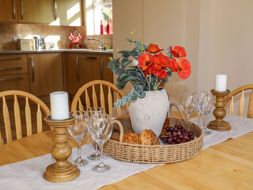 A dining table with wooden chairs and a tray holding a vase with red flowers bread rolls grapes and empty wine glasses at Glan Y Don in Abersoch