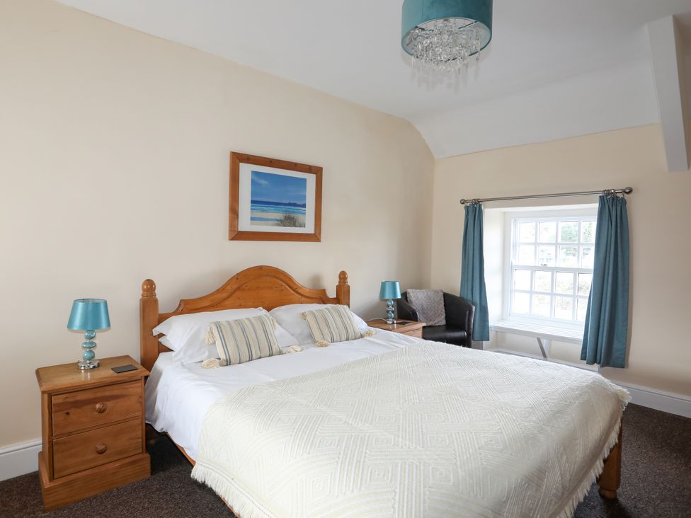A bedroom with a double bed wooden bedside tables lamps a window with blue curtains and a framed picture at Glan Y Don in Abersoch