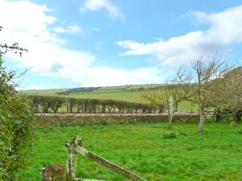 A grassy field with trees stone wall and a gate under a blue sky at The Carthouse in Shorwell