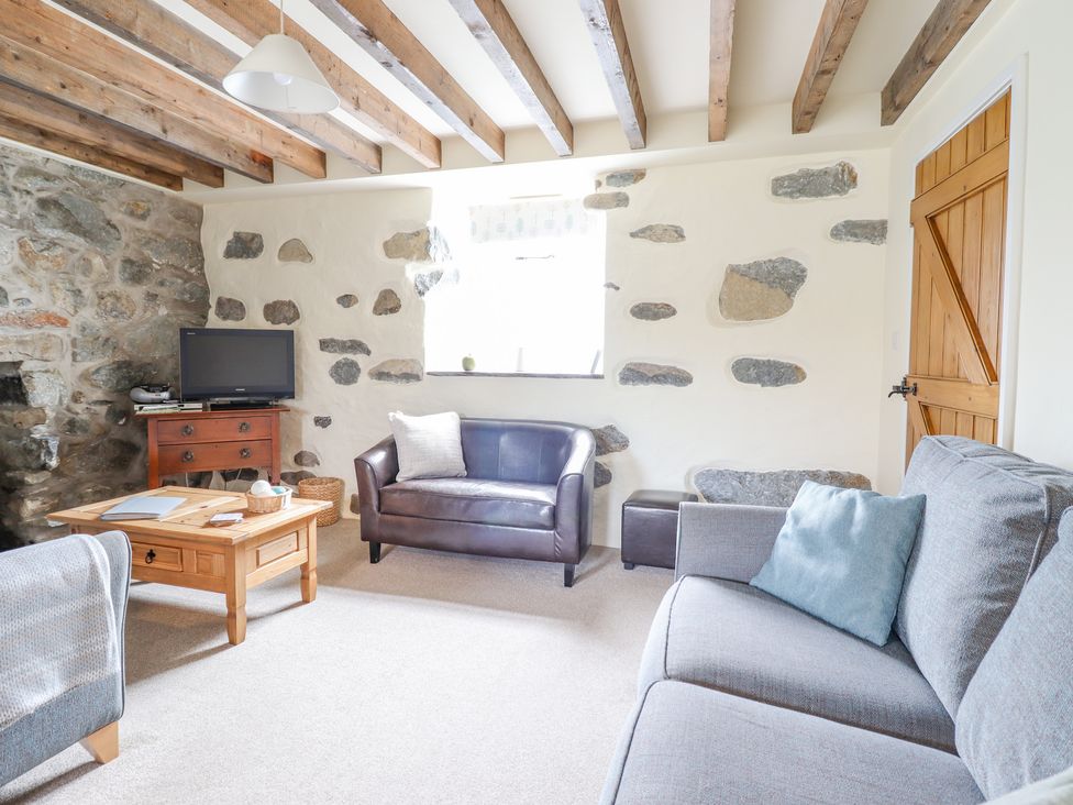 A living room with exposed wooden beams stone walls a gray sofa a brown leather loveseat a wooden coffee table and a television at Ysgybor Yd in Chwilog near Criccieth
