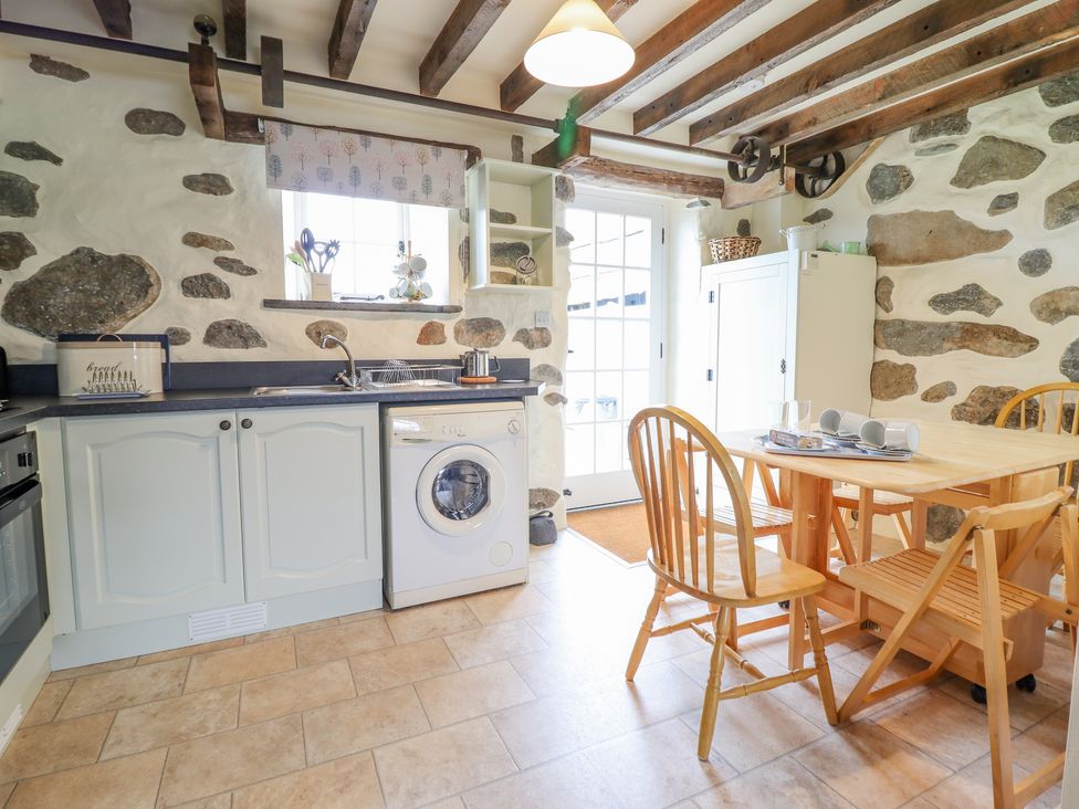 A kitchen with wooden dining table and chairs stone walls and exposed wooden beams at Ysgybor Yd in Chwilog near Criccieth