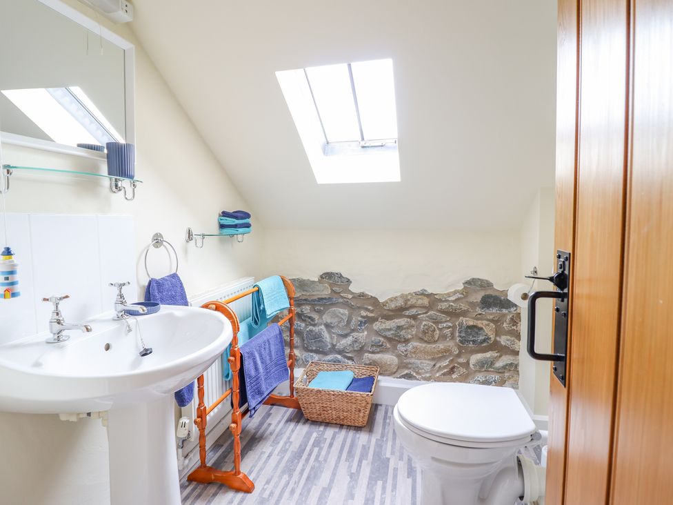 A bathroom with a white sink and toilet a wooden towel rack and a skylight at Ysgybor Yd in Chwilog near Criccieth