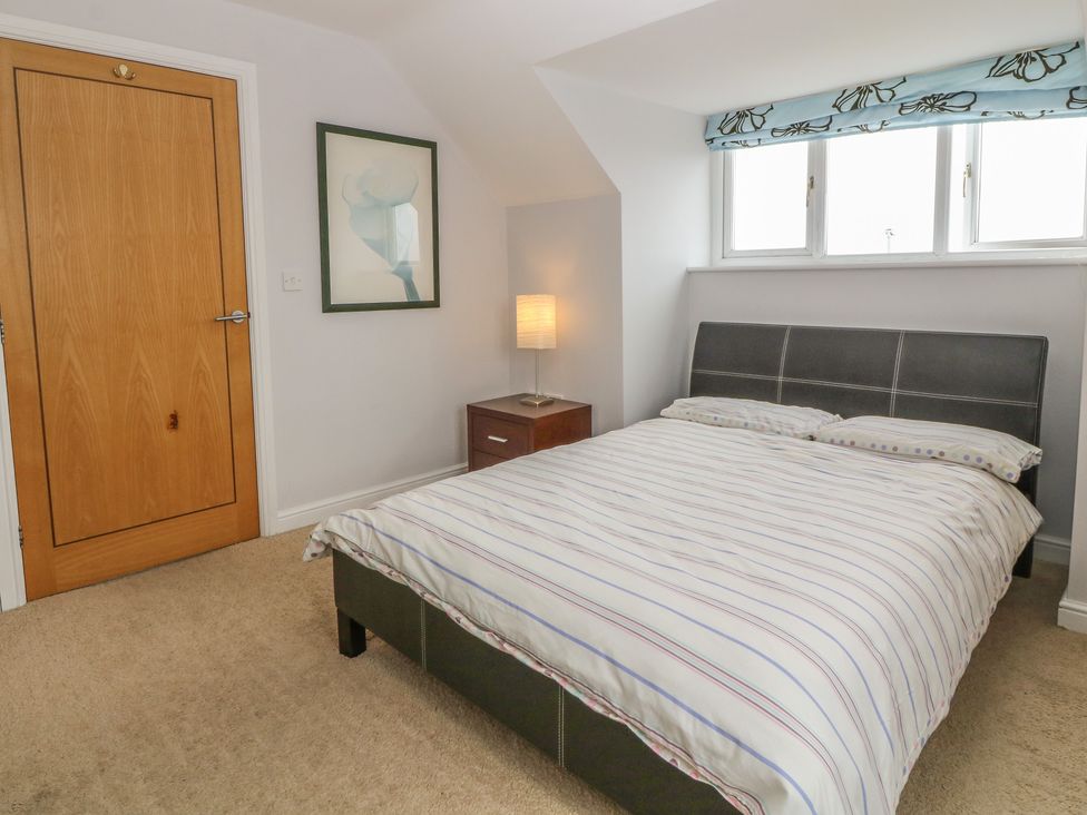 A bedroom with a bed a wooden door a bedside table with a lamp and a framed picture on the wall at 5 Cae Derwydd in Cemaes Bay