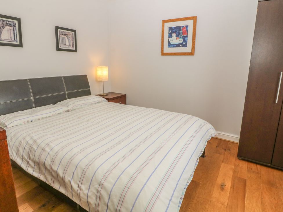 A bedroom with a bed with striped bedding a bedside table with a lamp framed pictures on the walls and a wardrobe at 5 Cae Derwydd in Cemaes Bay