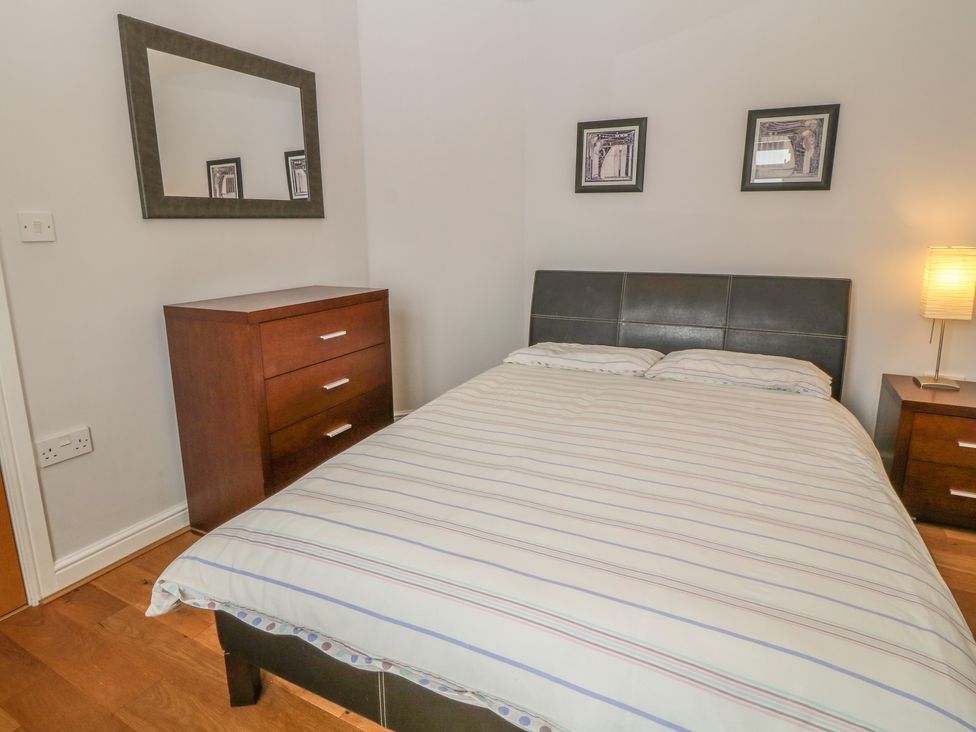 A bedroom with a bed a wooden dresser a bedside table with a lamp and framed pictures on the wall at 5 Cae Derwydd in Cemaes Bay