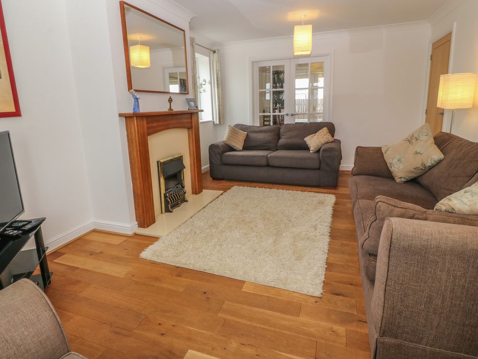 A living room with two sofas a fireplace a mirror a white rug and wooden flooring at 5 Cae Derwydd in Cemaes Bay