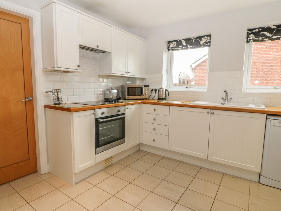 A kitchen with white cabinets wooden countertops oven stove microwave toaster kettle sink and two windows at 5 Cae Derwydd in Cemaes Bay