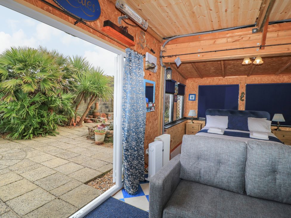 A room with a bed and sofa next to a glass door opening to a patio with plants at The Games Room in Bracklesham Bay