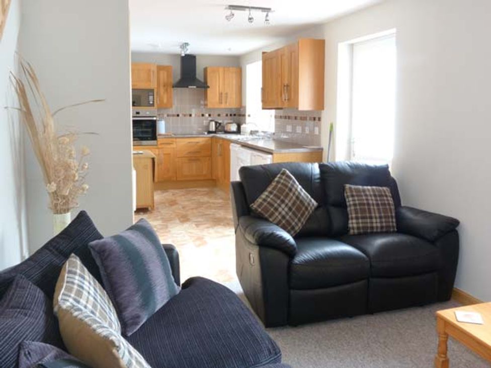 A living room with two sofas and cushions next to an open kitchen with wooden cabinets at The Croft House in Muir of Ord near Beauly