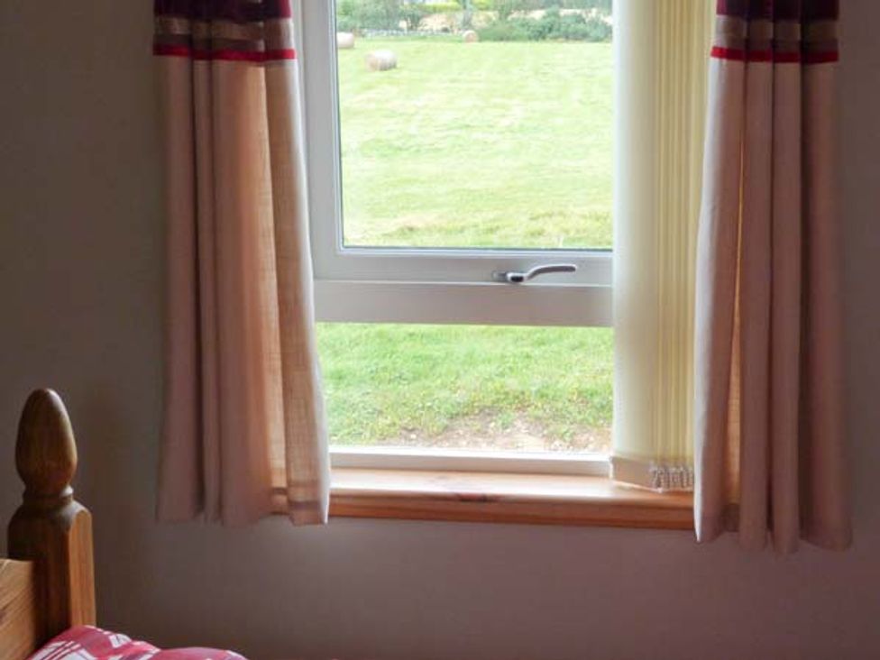 A window with curtains and a wooden bedpost visible in the corner at The Croft House in Muir of Ord near Beauly