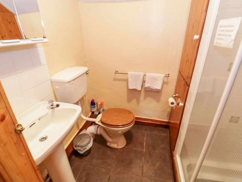 A bathroom with a sink toilet with wooden lid towel rack and shower at The Thatched Cottage in Drummin near Westport County Mayo