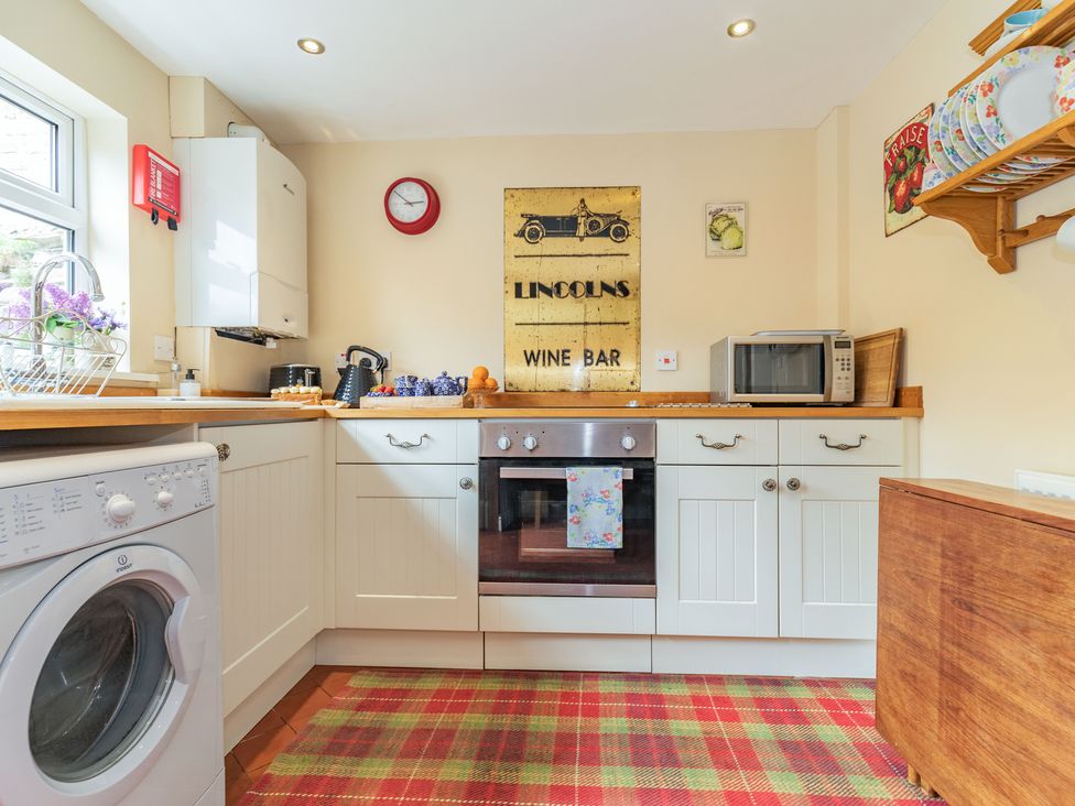 A kitchen with white cabinets a washing machine a microwave and a stove at Chapel Cottage in Stillington near Easingwold and York