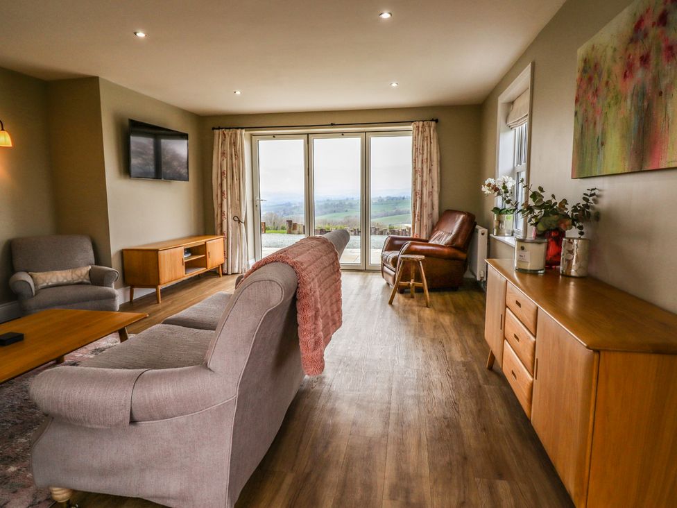 A living room with sofas coffee table and wooden sideboard with flowers at Red House Farm in Llanfair Caereinion near Welshpool