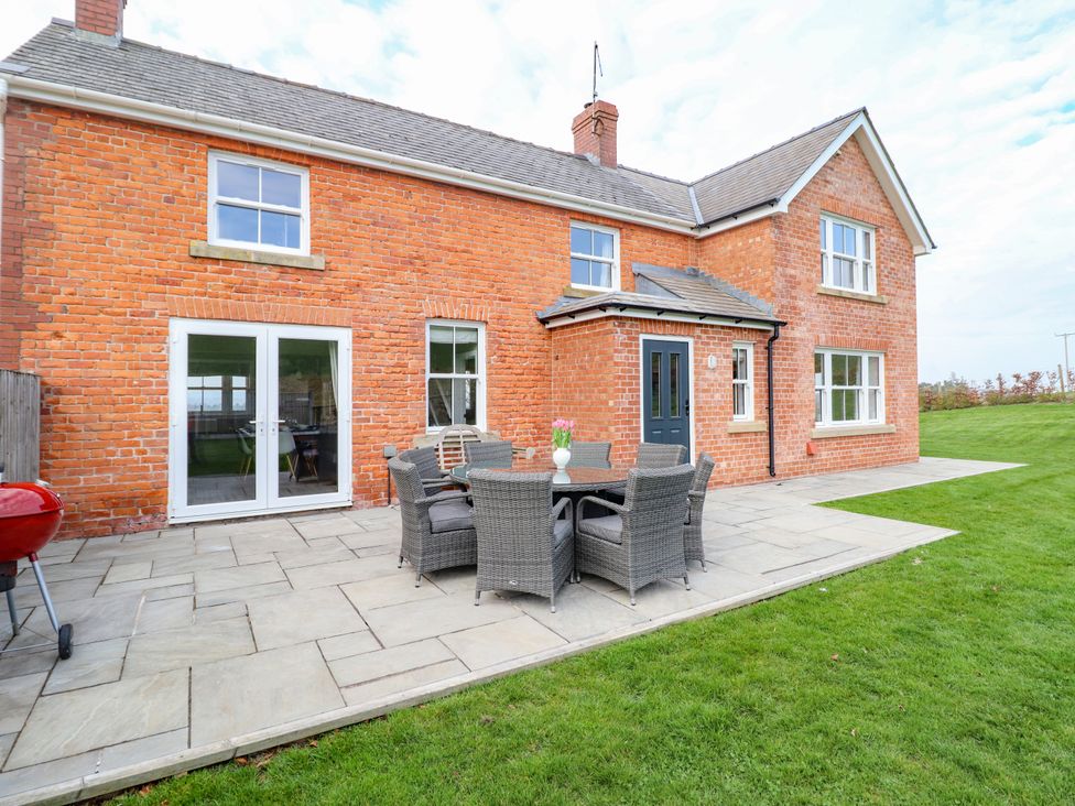 A patio with outdoor furniture and a brick house with windows and doors at Red House Farm in Llanfair Caereinion near Welshpool