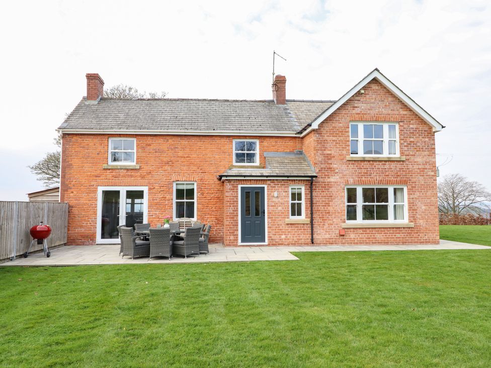 A brick house with a patio table and chairs on a stone terrace in a garden at Red House Farm Llanfair Caereinion near Welshpool