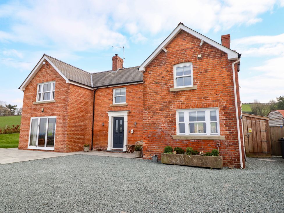 A red brick house with multiple windows and a dark front door with gravel in front at Red House Farm in Llanfair Caereinion near Welshpool