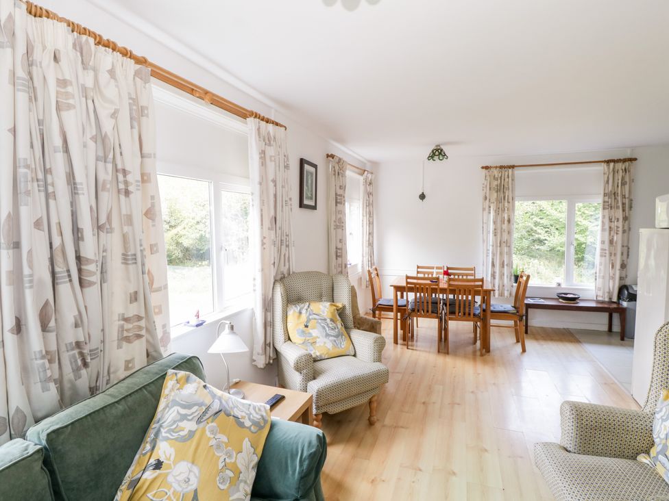 A living room and dining area with chairs and a table near windows with patterned curtains at Lakeside in Cahir near Ballinrobe County Mayo