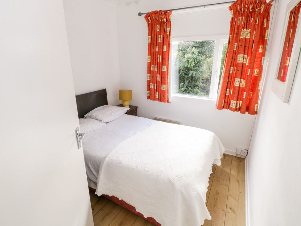 A small bedroom with a bed white bedspread bedside table with lamp window with orange curtains and wooden floor at Lakeside in Cahir near Ballinrobe County Mayo