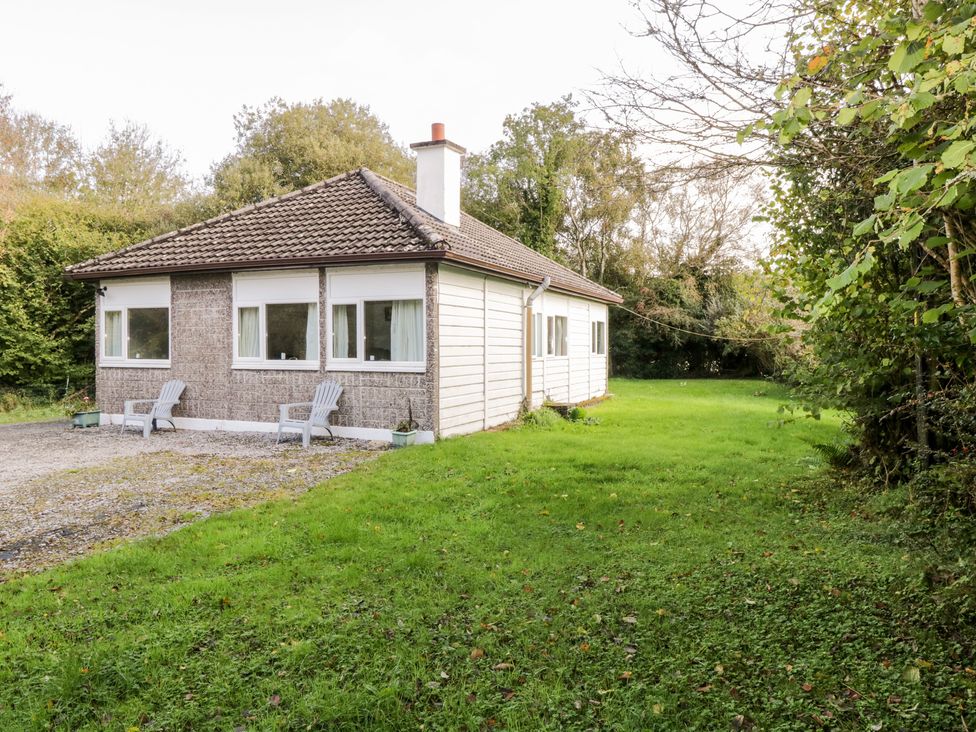 A single story house with two chairs outside on gravel and surrounded by grass and trees at Lakeside in Cahir near Ballinrobe County Mayo
