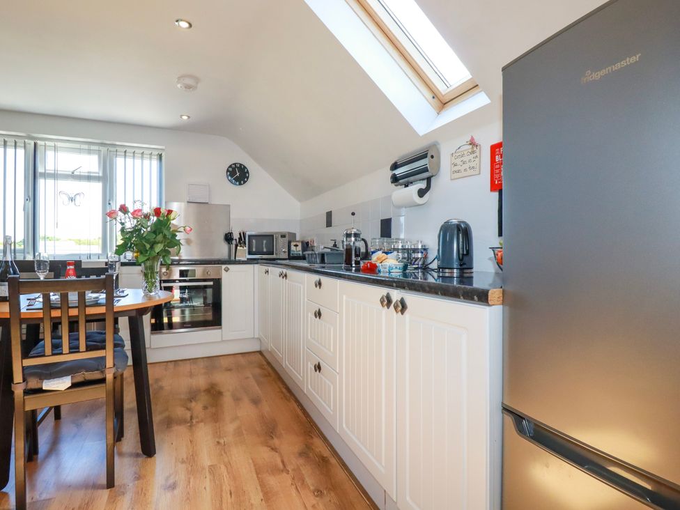 A kitchen with white cabinets a dining table with flowers and a refrigerator at Sunnyvale in Bugle near St Austell