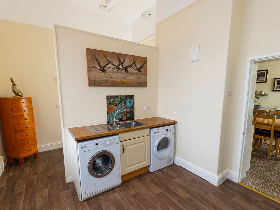 A utility room with a washing machine, dryer, sink, and wooden cabinet with a rabbit sculpture at Roa Island House in Roa Island