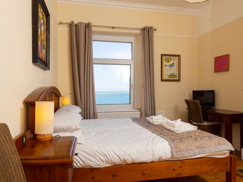 A bedroom with a wooden bed a window with curtains and a desk with a chair and television at Roa Island House Roa Island