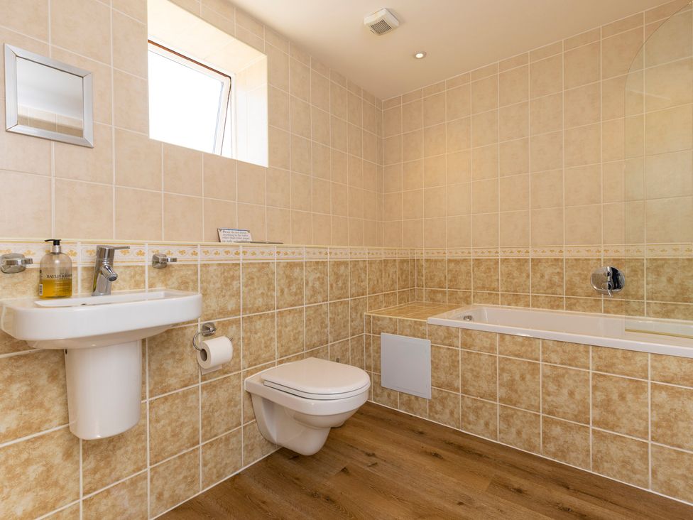 A bathroom with a wall-mounted toilet sink and bathtub with tiled walls and wooden floor at Roa Island House in Roa Island