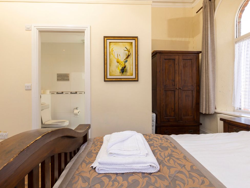 A bedroom with a wooden bed, folded towels on the bed, a wooden wardrobe, a window with curtains, and a view into a bathroom at Roa Island House in Roa Island