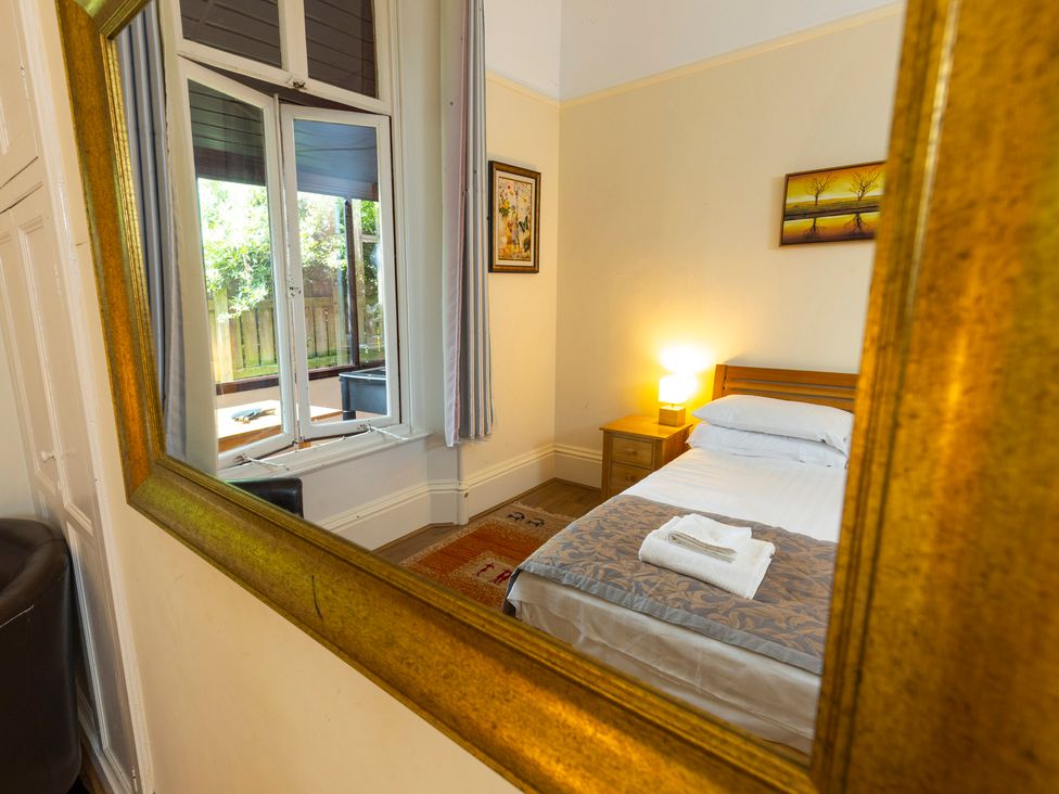 A bedroom with a bed and bedside table reflected in a large mirror at Roa Island House in Roa Island