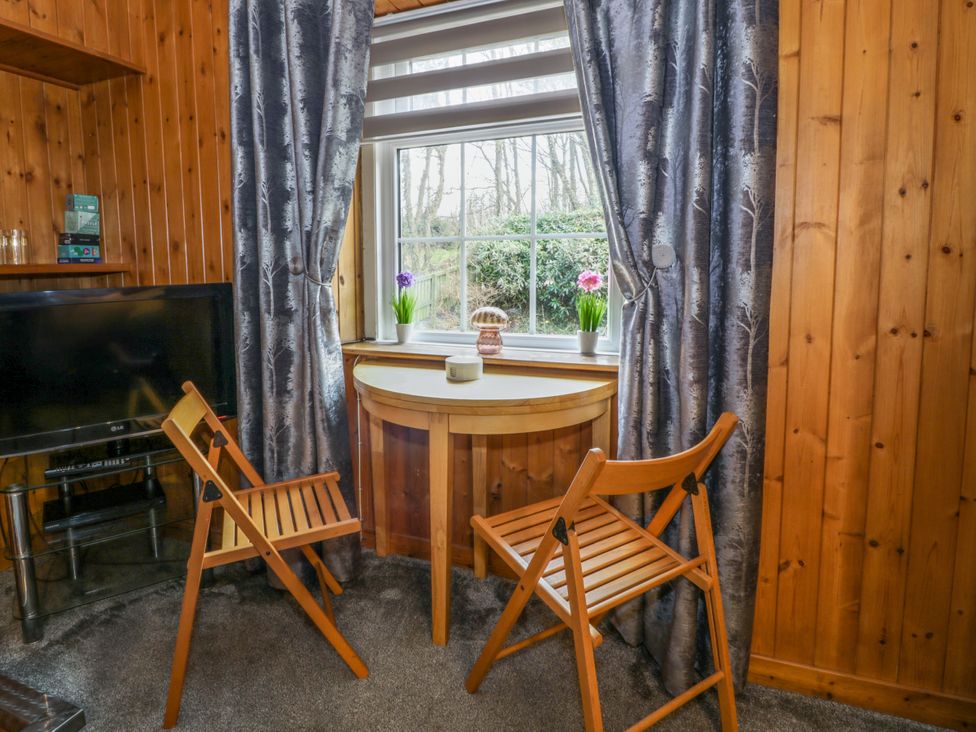 A corner with a small wooden table and two wooden folding chairs near a window with curtains and a television on a stand at Rose Cottage in Stranraer