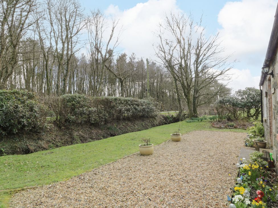 An outdoor area with gravel path, grass lawn, potted plants, and trees near a stone building at Rose Cottage in Stranraer