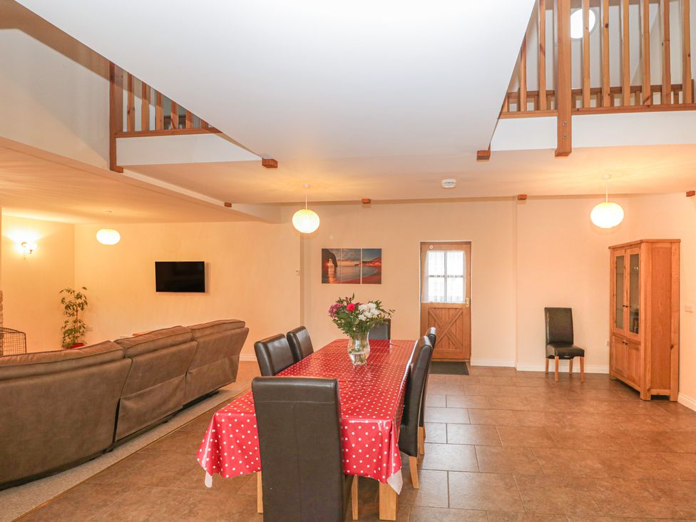 A dining room with a red polka dot tablecloth on the table and a sitting area with a brown sofa at The Old Barn in Harman's Cross near Swanage