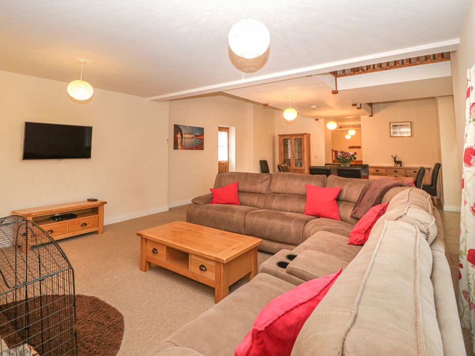A living room with sectional sofas red cushions wooden coffee table and a wall-mounted tv at The Old Barn in Harman's Cross near Swanage