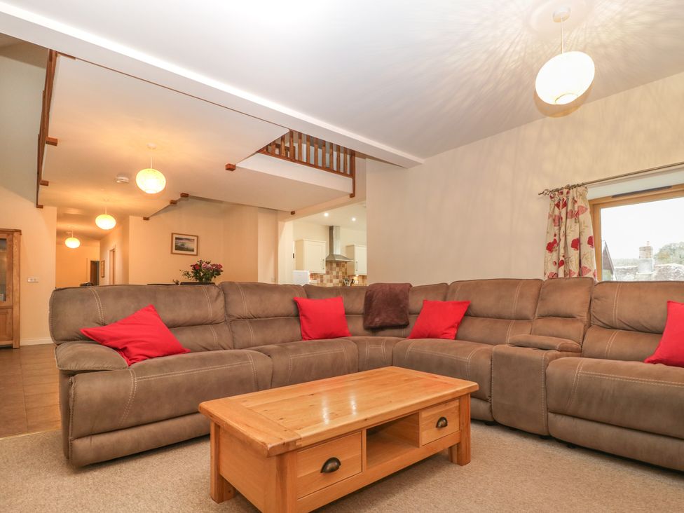 A living room with a brown sectional sofa and red pillows with a wooden coffee table at The Old Barn in Harman's Cross near Swanage